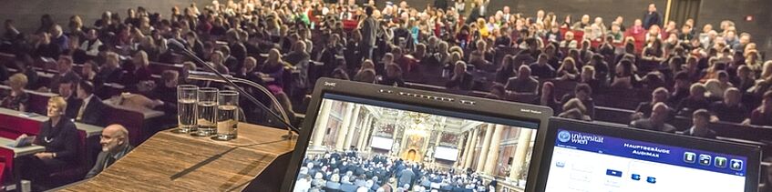 Rednerpult mit eingeschalteten Displays vor vollbesetztem Hörsaal