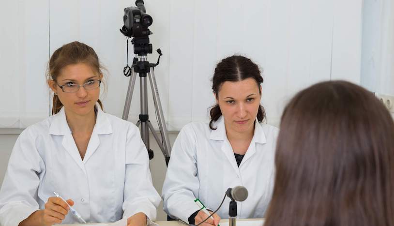 Zwei ernst blickende Frauen in weißen Kitteln interviewen Studienteilnehmerin